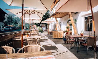 A cozy café with terrace chairs and sun umbrellas. The streets are quiet, and there are plants for decoration.
