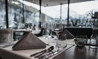 An elegantly set table in a restaurant with a view of the snowy mountains. The atmosphere is cozy and inviting. | © Verwöhn- & Wellnesshotel Walserhof| Frank Simon