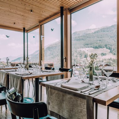 A modern restaurant with large windows and a view of the mountains. The tables are elegantly set, creating an inviting atmosphere. | © Naturhotel Chesa Valisa | Heldentheater