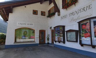 A charming building with blooming window boxes. It houses a salon and a drugstore. | © Kleinwalsertal Tourismus