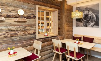 A cozy restaurant with wooden paneling and warm lighting. Tables and chairs invite you to linger, while a piece of art on the wall complements the atmosphere. | © Schönegger Käse-Alm