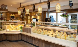 A cozy cheese shop with a variety of cheeses. The warm wooden tones and stylish lighting create an inviting atmosphere. | © Schönegger Käse-Alm