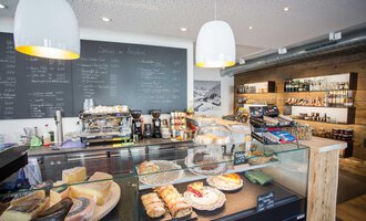 A modern café with a selection of baked goods and a sales counter. In the background, beverage and food shelves are visible. | © Kleinwalsertal Tourismus | Frank Drechsel