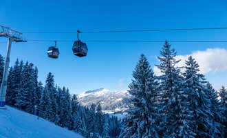 Eine schneebedeckte Berglandschaft mit Tannenbäumen und einer Gondelbahn. Der Himmel ist klar und blau. | © OBERSTDORF · KLEINWALSERTAL BERGBAHNEN