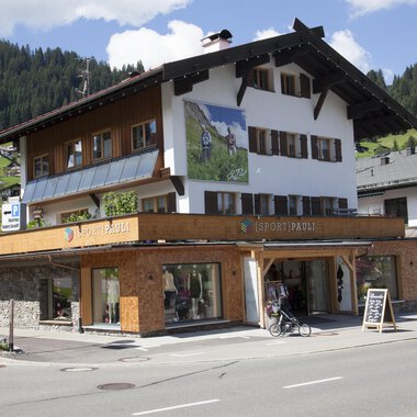 Ein traditionelles Alpenhaus mit Holzverkleidung und großen Fenstern. Im Vordergrund befindet sich ein Fahrrad und ein Informationsschild. | © Sport Pauli Matthias Bischof e.U