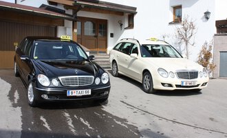 Zwei Taxis stehen vor einem Gebäude. Das schwarze Taxi ist eine Limousine und das weiße Taxi ein Kombi. | © Taxi Beranek | Elmar Beranek