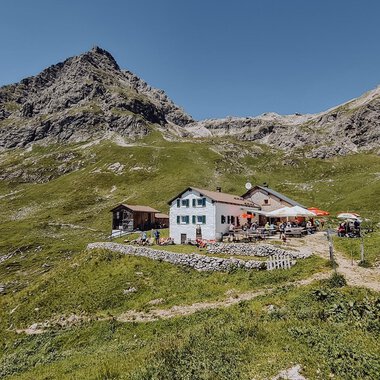 Ein malerisches Bergrestaurant umgeben von grünen Wiesen und Bergen. Der klare Himmel bietet eine schöne Kulisse für den Ort. | © Widdersteinhütte  | Vanessa Wüstner
