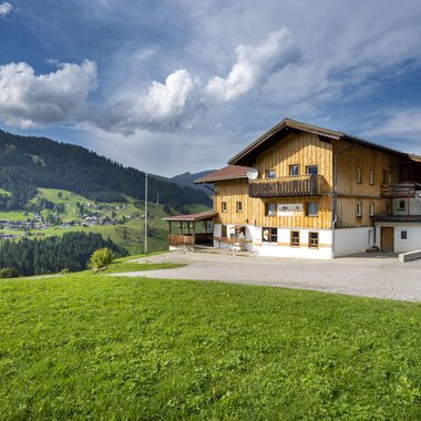 Ein wunderschönes Holzhaus in den Bergen mit grünen Wiesen. Der Himmel ist teilweise bewölkt und die Landschaft wirkt friedlich. | © Wildentalhütte | Theodor Pinn