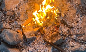 Ein gemütliches Lagerfeuer in einem Steinkreis. Die Flammen leuchten hell und erzeugen eine warme Atmosphäre. | © Wildnisschule Kleinwalsertal