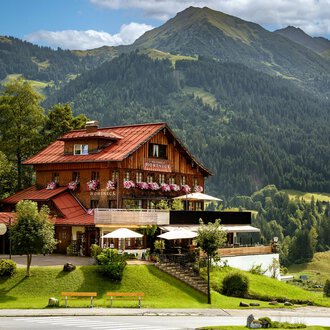 A picturesque chalet in the mountains with blooming flower boxes. In the background, green hills and majestic mountains rise.