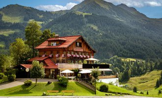 A picturesque chalet in the mountains with blooming flower boxes. In the background, green hills and majestic mountains rise.