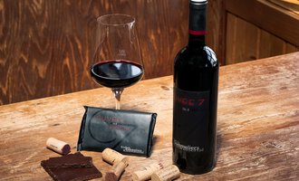 A red wine in a bottle with a glass beside it, surrounded by chocolate and corks on a wooden table. Ideal for a relaxing evening. | © Wirtshaus Hoheneck | Klaus Ruland