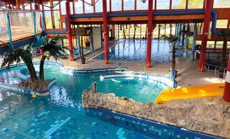 A colorful indoor swimming pool with various pools and a tropical atmosphere. Palms and rocks create a relaxing ambiance. | © WONNEMAR