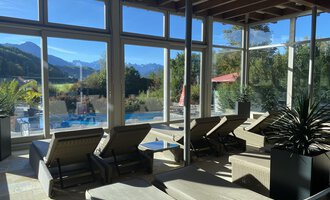 A tranquil wellness area with loungers and large windows. In the background, mountains and a pool can be seen. | © WONNEMAR Sonthofen | Julia Sondergelt
